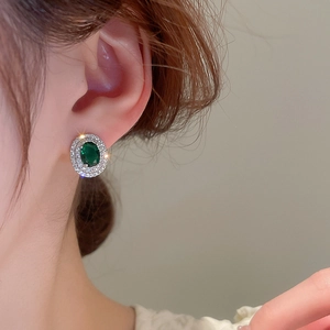 Close-up of a vintage emerald green stud earring with brilliant zircon halo on a model