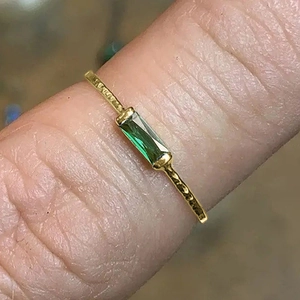 Detailed close-up of a slim gold ring featuring an emerald-cut green gemstone on a finger