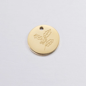 Detailed view of a golden circular pendant featuring an engraved holly leaf and berry design