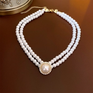 Détail d'un collier double épaisseur doré avec perles blanches et pendentif diamant