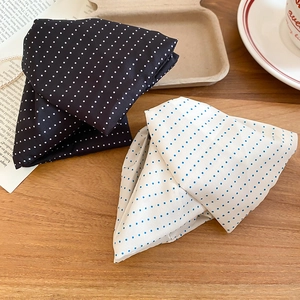Detailed view of polka dot fabric triangle hair clips in black and cream on a wooden desk