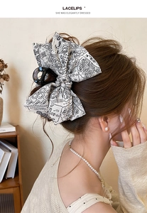 Detailed back view of a large cream paisley bow hair claw clip styled on wavy brunette hair