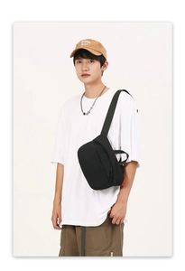 Detail of black nylon crossbody bag with orange brand tag and sturdy wide strap
