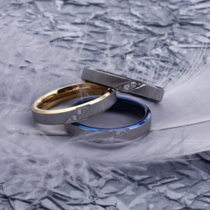 Brushed stainless steel rings with diamonds in gold, blue, and black on a white feather