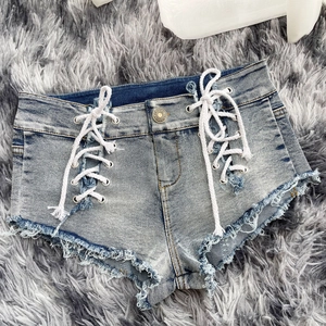 Dettaglio degli shorts in denim azzurro con lacci laterali e orlo a frange su tappeto