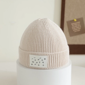 Detail of cream ribbed knit kids hat with fashion alphabet label on display stand