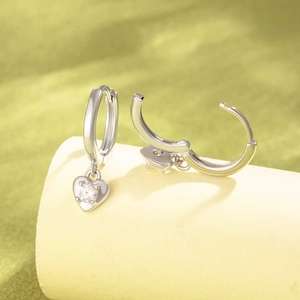 Boucles d'oreilles cœur en zircon argenté sur un présentoir cylindrique épuré