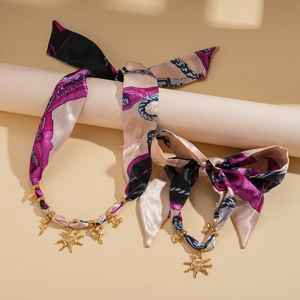 Detail of pink and black floral silk scarf necklace with gold sun and angel charms