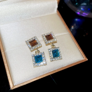Gros plan sur des boucles d'oreilles carrées avec gemmes ambre et bleues en écrin