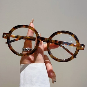 Détail de montures de lunettes de soleil rondes rétro en écaille tenues sur fond neutre
