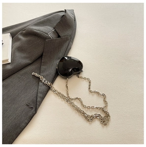 Detail of a black heart-shaped crossbody bag with faceted geometric surface and silver chain
