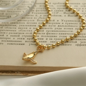 Macro detail of a gold whale tail pendant on a bead chain over a book page