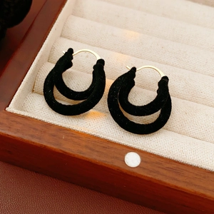 Détail de boucles d'oreilles doubles en velours noir avec crochets dorés dans un écrin