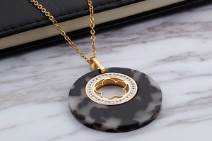 Close-up of gold clover pendant with resin pattern and diamond-set circular frame