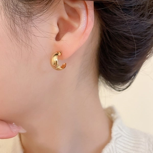 Detailed close-up of golden C-shaped earring with polished finish on model's ear
