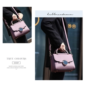 Detail of mauve pebbled leather handbag with round metal lock and textured handle