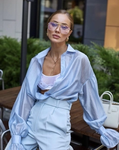 Detail of light blue sheer shirt paired with high-waisted trousers and white handbag
