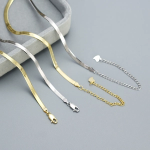 Flat snake bone necklaces in gold and silver finish on a premium grey velvet jewelry tray