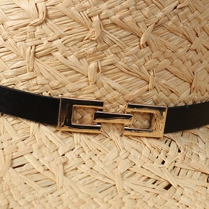 Detail of raffia sun hat featuring natural weave textures and a golden buckle on black band