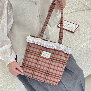 Detail of vintage plaid tote bag with white lace trim and Happy patch on a soft sofa