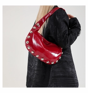 Close-up of red patent leather shoulder bag with silver studs on a model's shoulder
