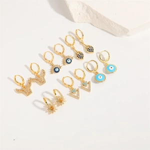 Detailed close-up of golden Evil Eye and geometric star earrings with blue zircon stones