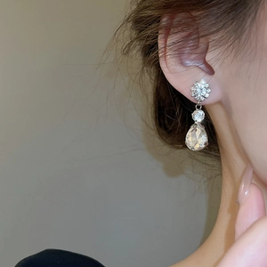 Detailed close-up of silver drop earrings with floral crystal studs on female model