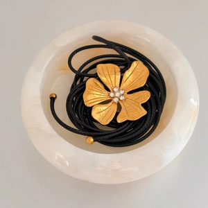 Macro detail of a gold flower pendant with sparkling crystals on black braided rope cord