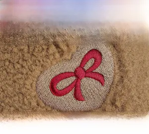 Detail of heart and bow embroidery on warm camel brown faux shearling baseball cap