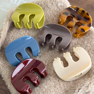 Glossy M-shaped acrylic hair claws in assorted colors on soft beige knitwear