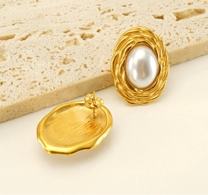 Detail of vintage gold twisted metal earrings with large oval pearl inlays on marble