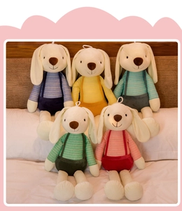 Detail of five plush long-eared rabbits wearing colorful striped overalls on a bed