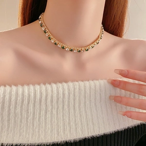 Close-up of a gold necklace with green and white gems worn by a model on a collarbone
