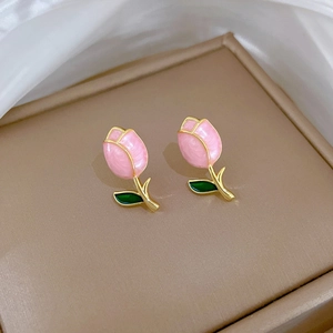 Macro detail of tulip earrings with pink enamel petals and gold stems on a jewelry box