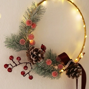Golden Christmas wreath with pine needles, red berries, pine cones and warm LED lights