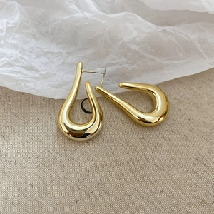 Macro shot of polished gold-finished C-shape metal earrings on a natural linen fabric