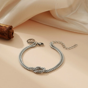 Silver double chain bracelet with woven knot design on beige silk background