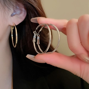 Close-up of minimalist large silver hoop earring held by hand to show sleek metal finish