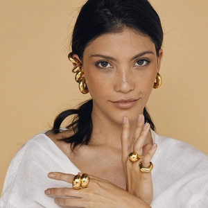 Gros plan de boucles d'oreilles dorées en C et de bagues géométriques sur un mannequin