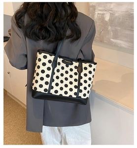 Close-up of polka dot canvas tote bag with black leather straps and metal brand logo