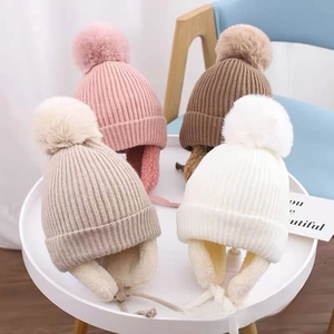 Detailed view of warm knit earflap hats with pom-poms in pink, coffee, and beige colors