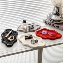 Close-up of wavy ceramic jewelry trays in black, silver, beige and red finishes