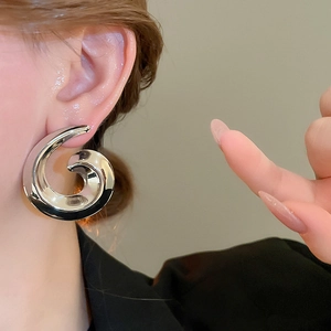 Close-up of a model wearing large polished silver spiral stud earrings in a modern style
