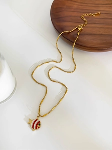 Detail of gold bead chain with red and white striped enamel fish pendant on white surface