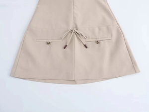 Detail view of beige skirt featuring drawstring waist and decorative button pockets