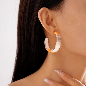 Detailed view of orange gradient woven C-shaped earrings on model for summer style