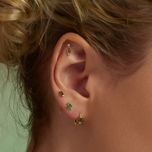 Close-up of green gemstone earrings set in gold, including studs and hoop on a model ear