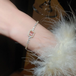 Close-up of rose gold bracelet with pink rectangular zircon on a feathered sleeve