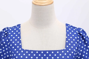 Close-up of the square neckline and shoulder pleat details on the blue polka dot dress
