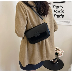 Detail view of a black leather crossbody bag with elegant gold buckle on a stylish model